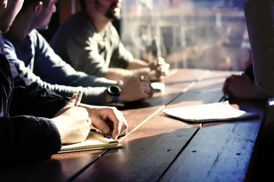 people sitting on chair in front of table while holding pens during daytime